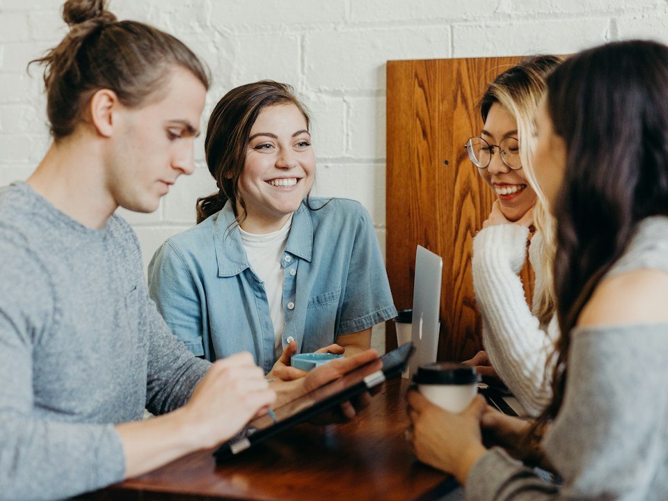 Grupo de estudiantes sonrientes compartiendo material en una mesa; fotografía ilustrativa